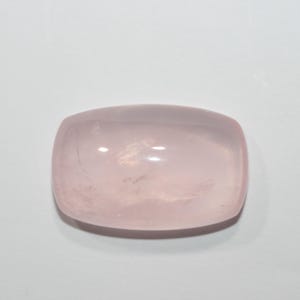 Puede incluir: Una gema de cuarzo rosa pulida, rectangular con esquinas redondeadas. La piedra tiene un tono rosa suave y translúcido y una superficie lisa y reflectante. La gema está sobre un fondo blanco.