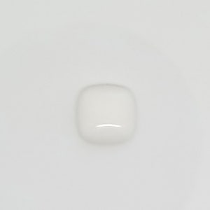 Könnte beinhalten: Ein kleines, weißes, quadratisch geformtes Objekt mit abgerundeten Ecken. Das Objekt hat eine glänzende Oberfläche und eine subtile, gebogene Vertiefung auf einer Seite, die das Licht reflektiert. Der Hintergrund ist eine schlichte weiße Oberfläche.