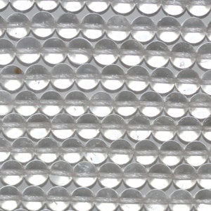 Puede incluir: Primer plano de cuentas de cristal de cuarzo transparente. Las cuentas redondas están dispuestas en filas, ensartadas juntas. Las cuentas transparentes reflejan la luz, creando un efecto brillante. Estas cuentas son una opción popular para la fabricación de joyas.