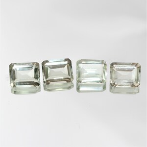Puede incluir: Cuatro piedras preciosas de corte rectangular de color verde esmeralda. Las piedras preciosas son facetadas y tienen un aspecto claro y vítreo.