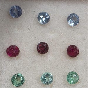 Può includere: Nove gemme rotonde nelle tonalità del blu, del rosso e del verde. Le gemme sono disposte in una griglia di tre per tre. Le gemme sono sfaccettate e sembrano essere su una superficie chiara.