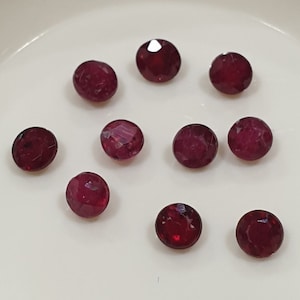Könnte beinhalten: Zehn runde, rote Edelsteine auf einer weißen Oberfläche. Die Edelsteine sind alle gleich groß und gleich geformt.