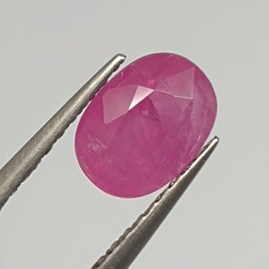 Può includere: Una pietra preziosa ovale di colore rosa con taglio a faccette. La pietra preziosa è tenuta in posizione da una pinzetta.