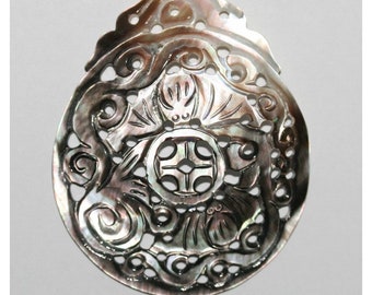 May include: A round, black and iridescent mother of pearl pendant with an intricate carved design. The design features a central cross with floral motifs surrounding it.