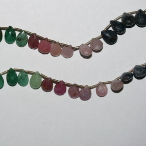 Op de afbeelding: Een streng edelsteen kralen in verschillende tinten groen, roze en blauw. De kralen zijn druppelvormig en geregen op een zilveren draad.