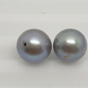 Könnte beinhalten: Zwei runde, irisierende graue Perlen mit einem Loch in der Mitte.