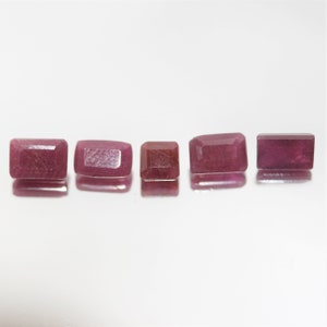 Könnte beinhalten: Fünf rosa rechteckige Edelsteine mit facettiertem Schliff. Die Edelsteine sind in einer Reihe auf einer weißen Oberfläche angeordnet.