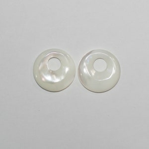 May include: Two white mother of pearl shell donut shaped beads with a hole in the center.