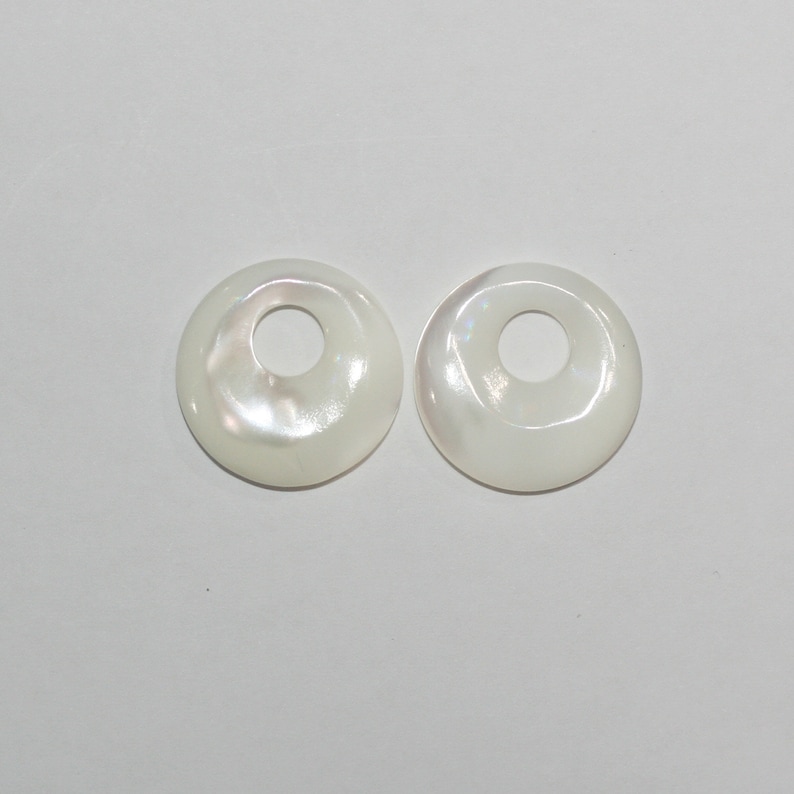 May include: Two white mother of pearl shell donut shaped beads with a hole in the center.