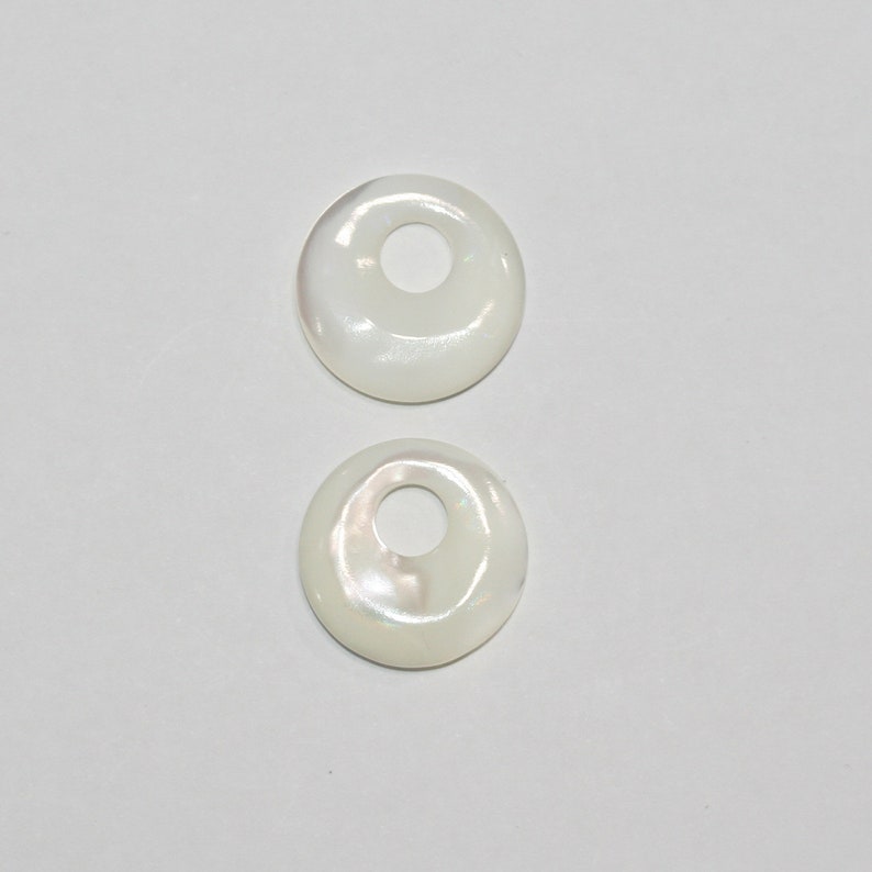 May include: Two white mother of pearl shell rings with a hole in the center. The rings are smooth and have a slight iridescent sheen.