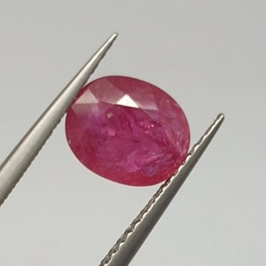 May include: A vibrant pink oval-shaped ruby gemstone held by tweezers.