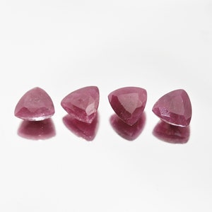 Può includere: Quattro pietre preziose triangolari rosa con bordi sfaccettati, esposte su una superficie bianca.