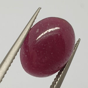 Può includere: Una pietra preziosa ovale cabochon rosa intenso con una superficie liscia e lucida.