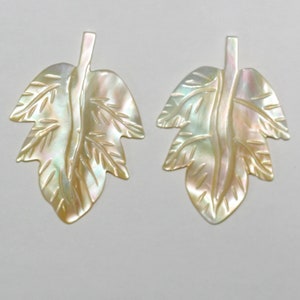 May include: Two iridescent white shell leaf-shaped pendants with a carved design.