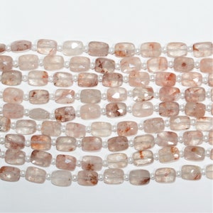 Pode incluir: Um fio de contas de quartzo transparente facetadas, retangulares, com inclusões vermelhas e laranja. As contas são enfiadas em um fio branco.