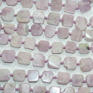 May include: Close-up of rows of light pink, square-cut gemstone beads strung on a purple cord. The beads have a slightly irregular shape and a polished surface, with variations in colour and texture. Ideal for jewellery making.