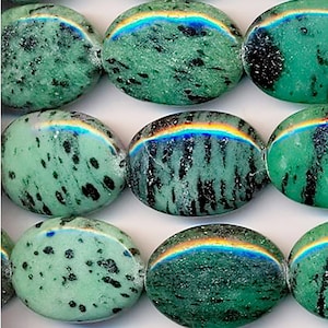 Pode incluir: Contas de pedra preciosa ovaladas de cor verde e preta com um brilho iridescente. As contas têm um padrão salpicado.