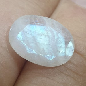 May include: A white oval moonstone with a blue iridescent sheen. The stone is smooth and polished.