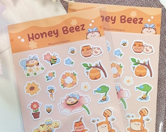 May include: Two sheets of stickers featuring a cute cartoon bee character. The stickers are on a pink background and feature various designs, including bees, flowers, honey pots, and honeycomb. The text "Honey Beez" is printed on the top of each sheet.
