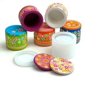 May include: Six small round painted boxes with lids. The boxes are decorated with colourful dots and patterns. The lids are also decorated with dots and patterns. The boxes are arranged in a pyramid shape.