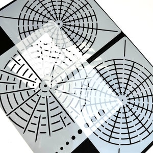 May include: Two black and white circular stencils with a grid pattern. The stencils are made of clear plastic and are designed for use with paint or other mediums.