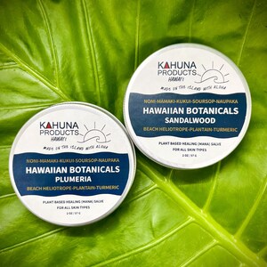 May include: Two silver containers with white labels and black text. The labels read "KAHUNA PRODUCTS HAWAII MADE ON THE ISLAND WITH ALOHA" and list ingredients. The containers are labelled "Hawaiian Botanicals Sandalwood" and "Hawaiian Botanicals Plumeria". Both containers are 2 oz / 57 g.