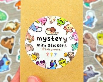 Puede incluir: Un sobre rectangular de papel marrón con una pegatina circular blanca que muestra ilustraciones de animales de dibujos animados. El texto dice mystery mini stickers @spicymochi con tres signos de interrogación en rojo, azul y amarillo.