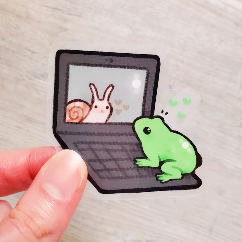 May include: A green frog looking at a laptop screen. The screen shows a pink snail with a brown shell. There are hearts floating around the snail.