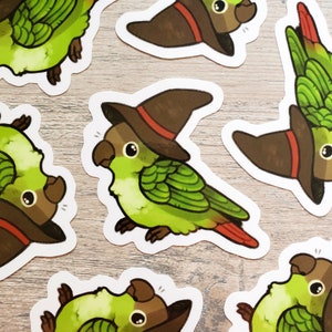 May include: A set of six stickers featuring green and brown parakeets wearing witch hats. The parakeets are depicted in various poses, with some looking directly at the viewer and others looking away. The stickers are printed on white paper and have a glossy finish.
