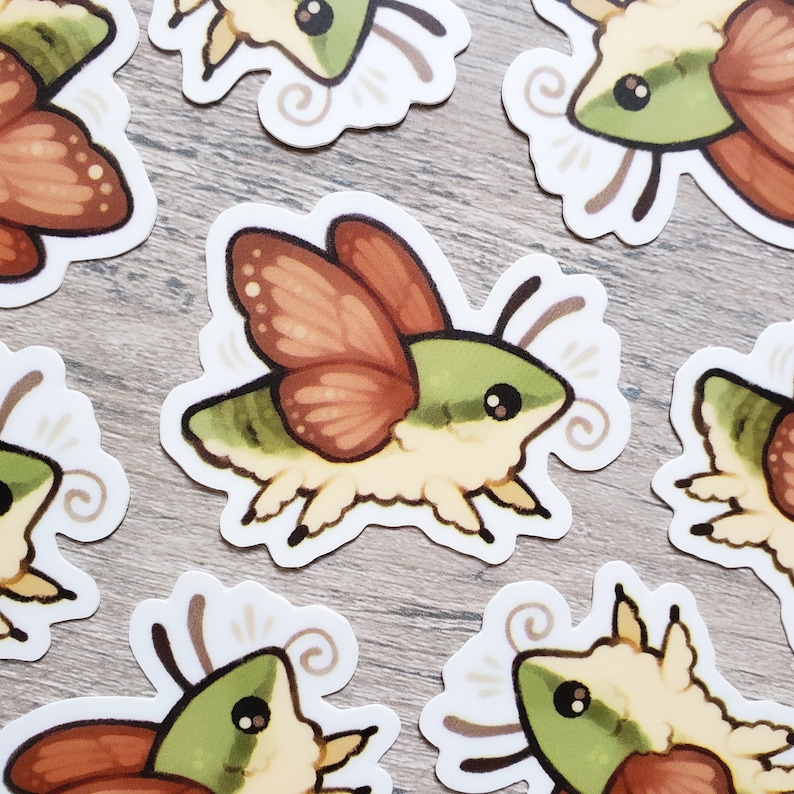 May include: A set of six stickers featuring a cartoon moth with green and brown wings. The moth has large, round eyes and a fluffy body. The stickers are printed on white paper and have a glossy finish.