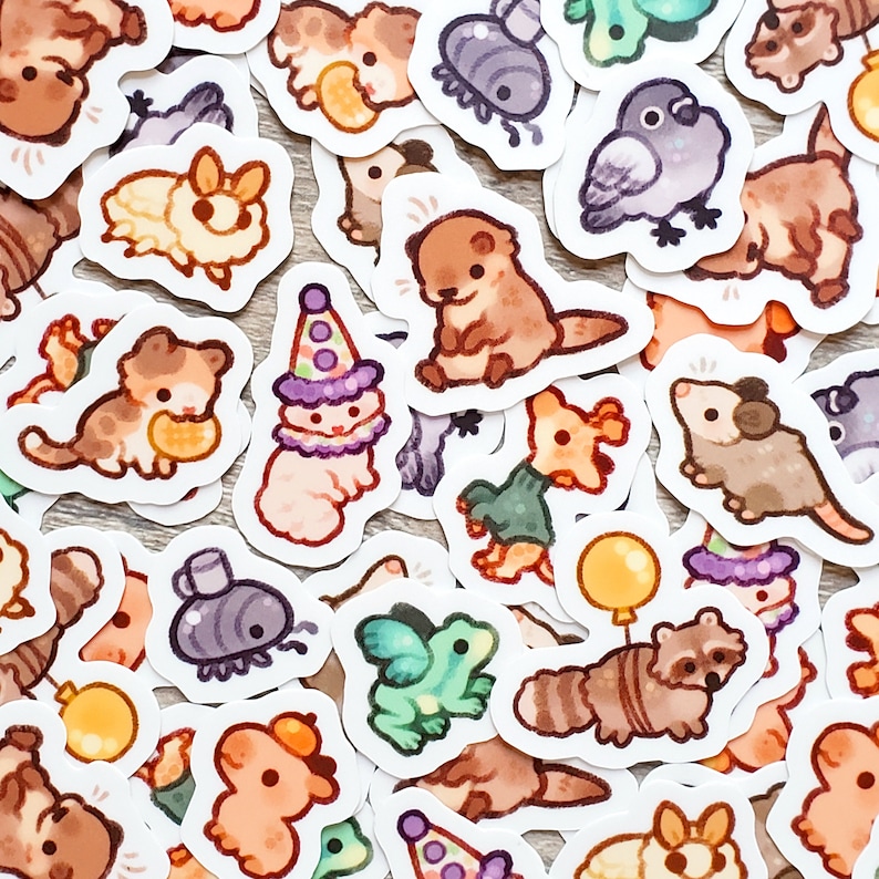 May include: A collection of colorful stickers featuring various animal and cartoon characters. The stickers are on a white background and include a variety of designs, such as a raccoon, a frog, a cat, a bear, and a bird.