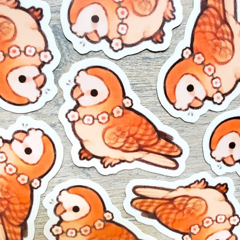 May include: A collection of stickers featuring cartoon owls in shades of orange and cream. Each owl has a floral necklace and black eyes. The stickers are arranged on a light grey surface.