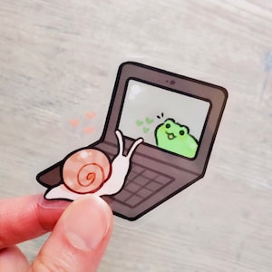 May include: A snail on a laptop computer screen video chats with a green frog. The snail is waving with its right hand and the frog is smiling. There are hearts floating around the frog.