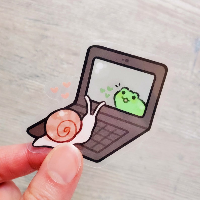 May include: A snail on a laptop computer screen video chats with a green frog. The snail is waving with its right hand and the frog is smiling. There are hearts floating around the frog.