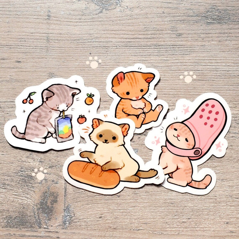 May include: Four adorable cartoon cat stickers with different designs. One cat is drinking juice, another is holding a loaf of bread, another is wearing a pink Croc, and the last one is sitting with its paws crossed.