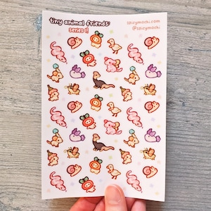 May include: A sheet of stickers featuring tiny animal friends in a variety of poses. The stickers are on a white background with pink accents. The text "tiny animal friends: series II" and "spicymochi.com @spicymochi" is printed on the sheet.