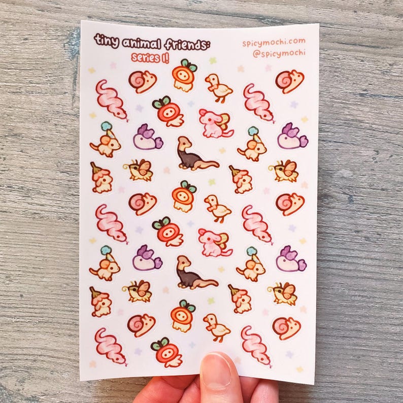 May include: A sheet of stickers featuring tiny animal friends in a variety of poses. The stickers are on a white background with pink accents. The text "tiny animal friends: series II" and "spicymochi.com @spicymochi" is printed on the sheet.