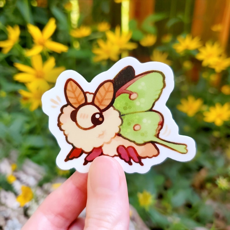 Pu&ograve; includere: Un adesivo colorato con una falena dei cartoni animati con un corpo soffice color crema, grandi occhi marroni e ali verdi. La falena ha antenne marroni e zampe rosse. L'adesivo &egrave; su sfondo bianco, con fiori gialli sullo sfondo.