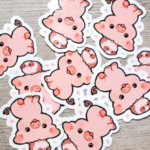 K&ouml;nnte beinhalten: Ein Set mit zehn rosa Schweinestickern, auf denen jeweils ein kleineres Schwein auf einem gr&ouml;&szlig;eren Schwein sitzt. Die Sticker befinden sich auf einer hellbraunen Holzoberfl&auml;che.
