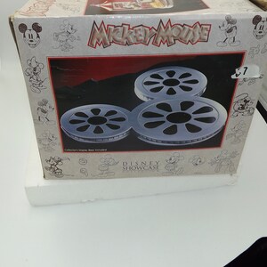 May include: A Mickey Mouse Disney Showcase box featuring three silver film reel sculptures. The box has a red and black background with the words "Mickey Mouse" in large letters. The box is white with Mickey Mouse illustrations.