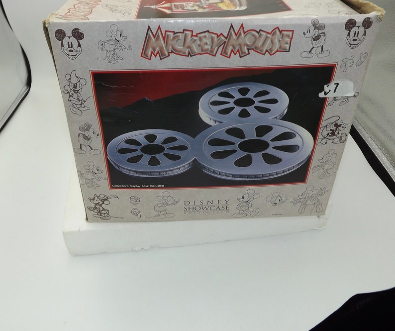 May include: A Mickey Mouse Disney Showcase box featuring three silver film reel sculptures. The box has a red and black background with the words "Mickey Mouse" in large letters. The box is white with Mickey Mouse illustrations.