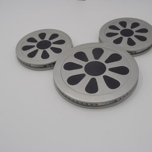 May include: Three silver-colored coasters arranged in a Mickey Mouse head shape. Each coaster has a black floral design in the center and a silver rim. The coasters are on a white background.