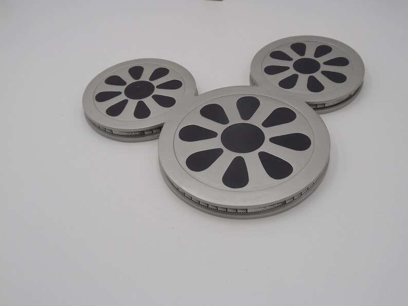 May include: Three silver-colored coasters arranged in a Mickey Mouse head shape. Each coaster has a black floral design in the center and a silver rim. The coasters are on a white background.