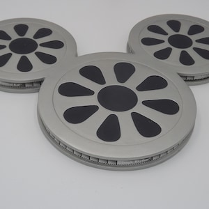 May include: Three gray, circular objects arranged in a Mickey Mouse head shape. Each has a black center and black petal-shaped designs. The text "Jungle Rhythm" is visible on the edge of each object. The objects are on a white surface.