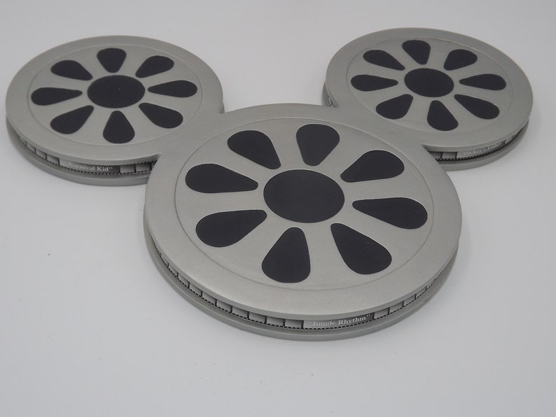 May include: Three gray, circular objects arranged in a Mickey Mouse head shape. Each has a black center and black petal-shaped designs. The text "Jungle Rhythm" is visible on the edge of each object. The objects are on a white surface.