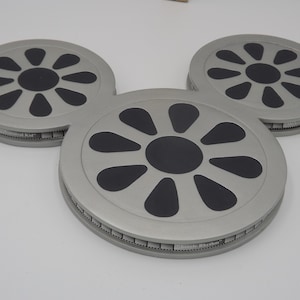 May include: Three gray, circular coasters arranged in a Mickey Mouse head shape. Each coaster has a black, stylized flower design in the center and the text "Musical Kid" and "Lunch Rhythm" on the sides.