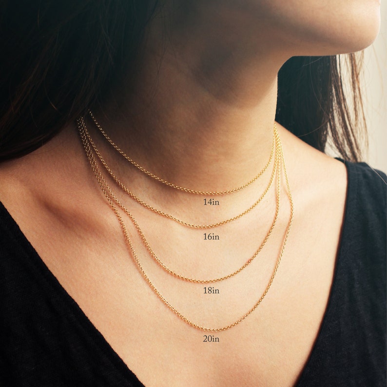 May include: Four gold chains of different lengths, 14 inches, 16 inches, 18 inches, and 20 inches, are layered on a person's neck. The chains are all the same style, a delicate, thin, cable chain.