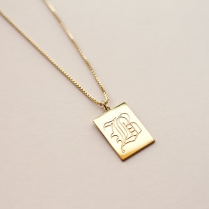 May include: A gold chain necklace with a rectangular pendant featuring a cursive letter 'B' engraved on it.