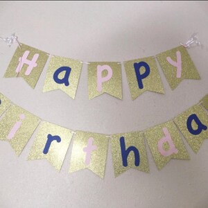 May include: Gold glitter banner with the words "Happy Birthday" in pink and navy blue letters.