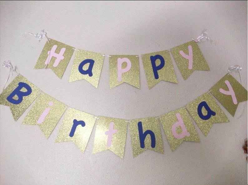 May include: Gold glitter banner with the words "Happy Birthday" in pink and navy blue letters.